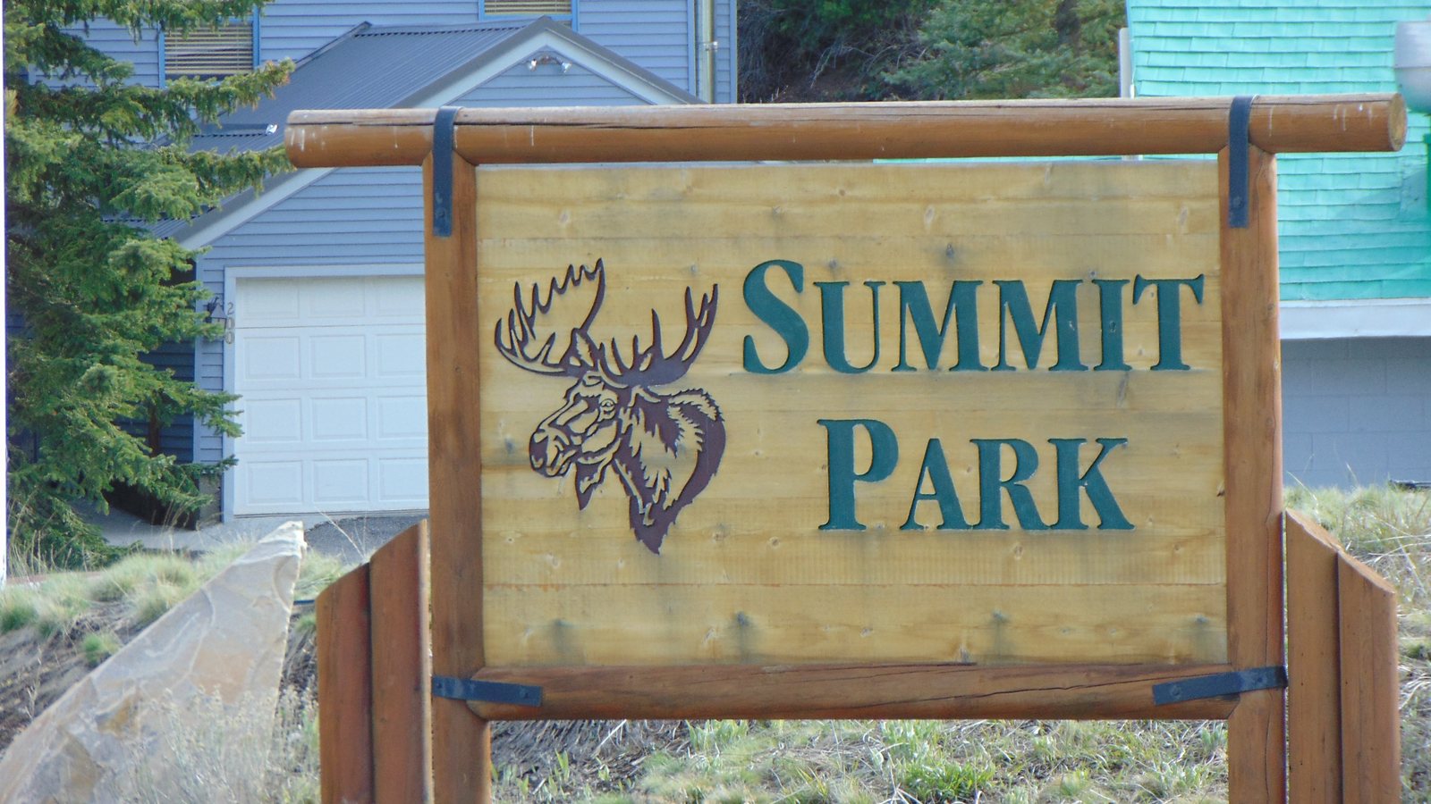 A wooden Summit Park sign with a carved moose head, in front of homes in Summit Park, Utah