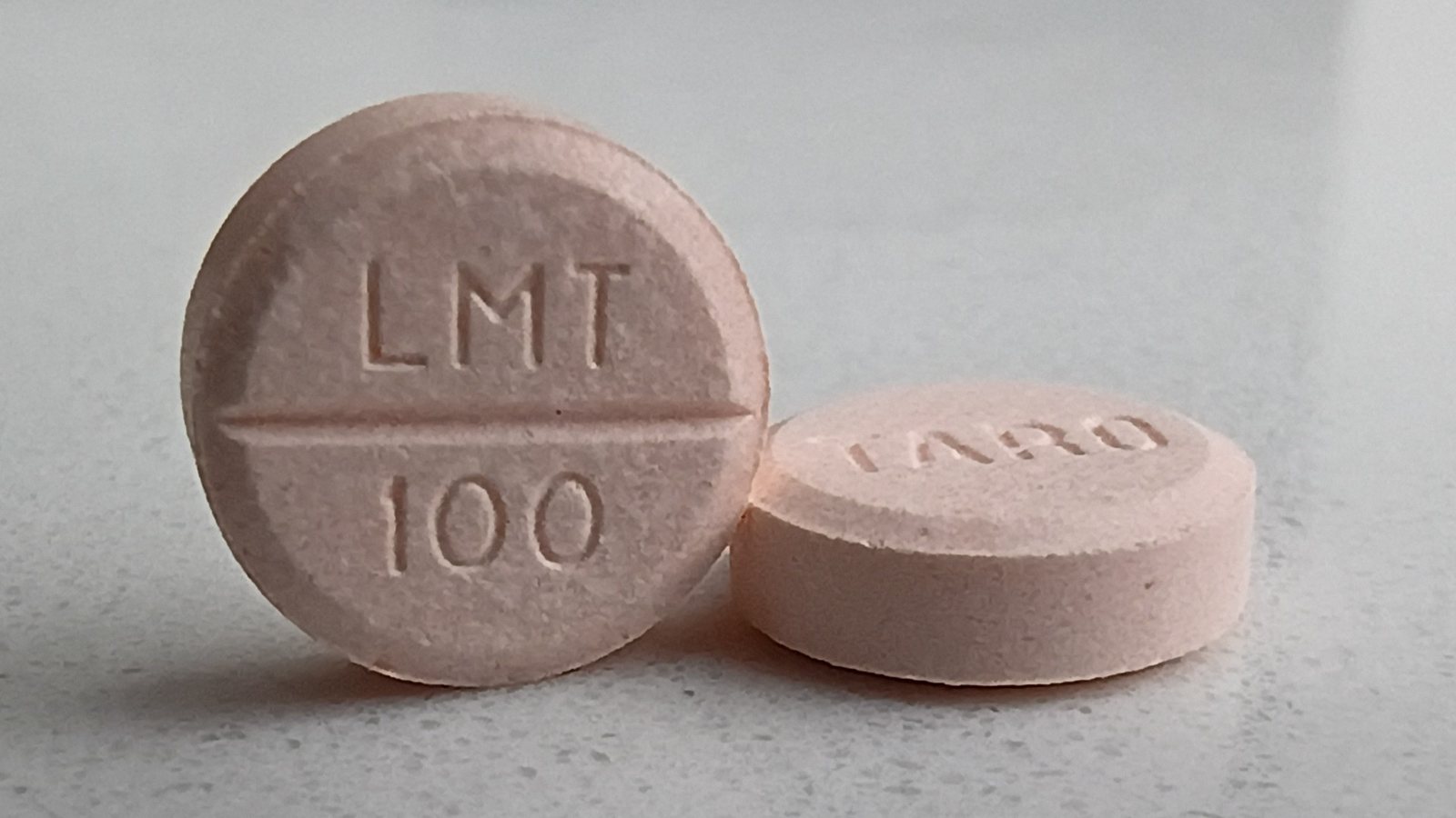Two peach-colored generic lamotrigine tablets stamped LMT 100 on a gray countertop