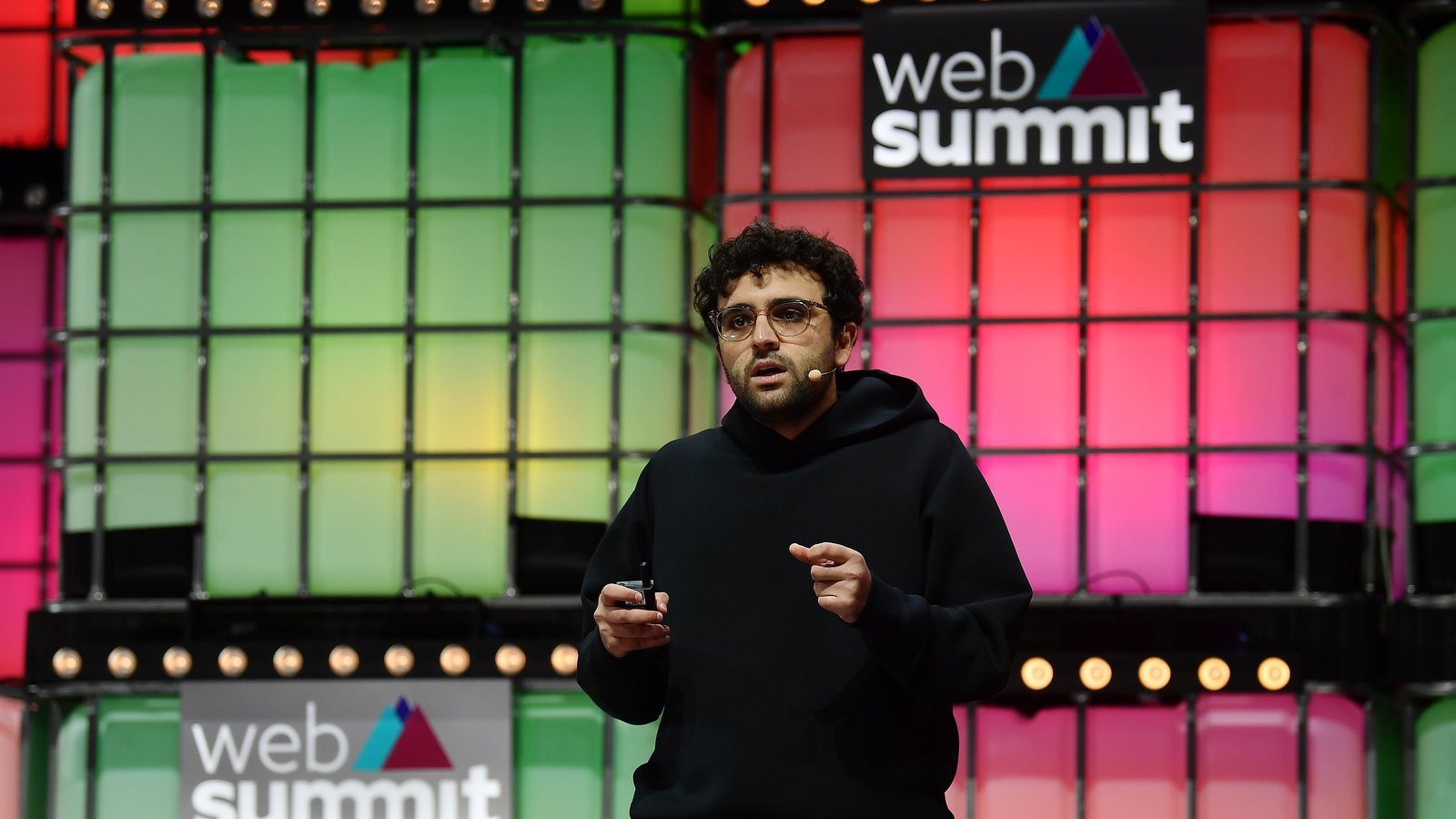 Kalshi co-founder Tarek Mansour in a black hoodie speaking on stage in front of a lit Web Summit backdrop