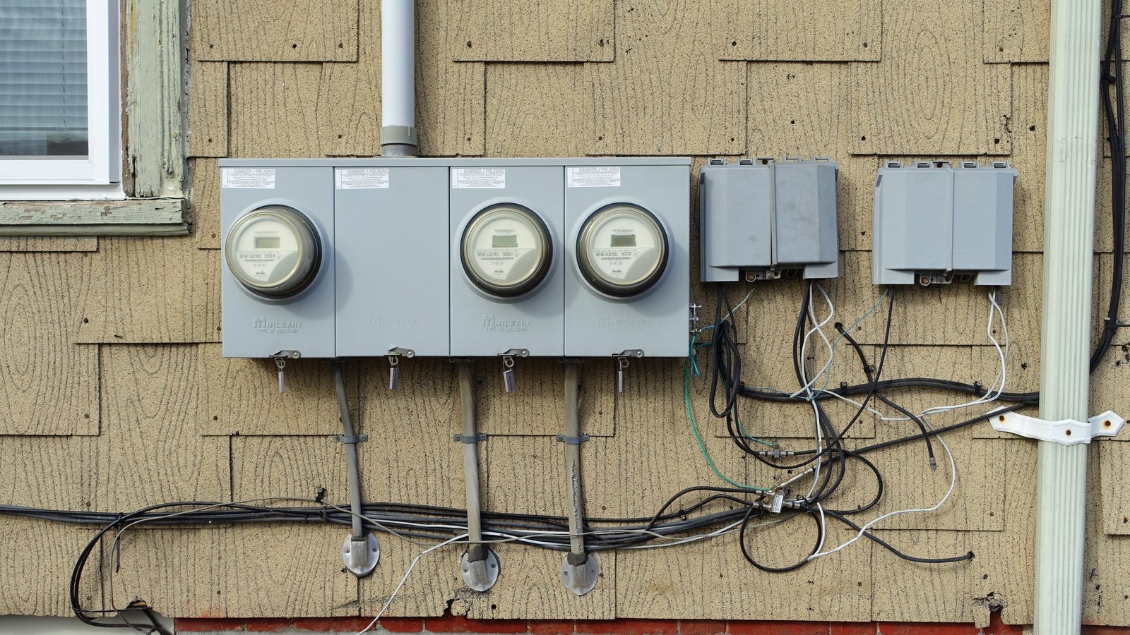 Three residential electric meters mounted on the shingled wall of a house