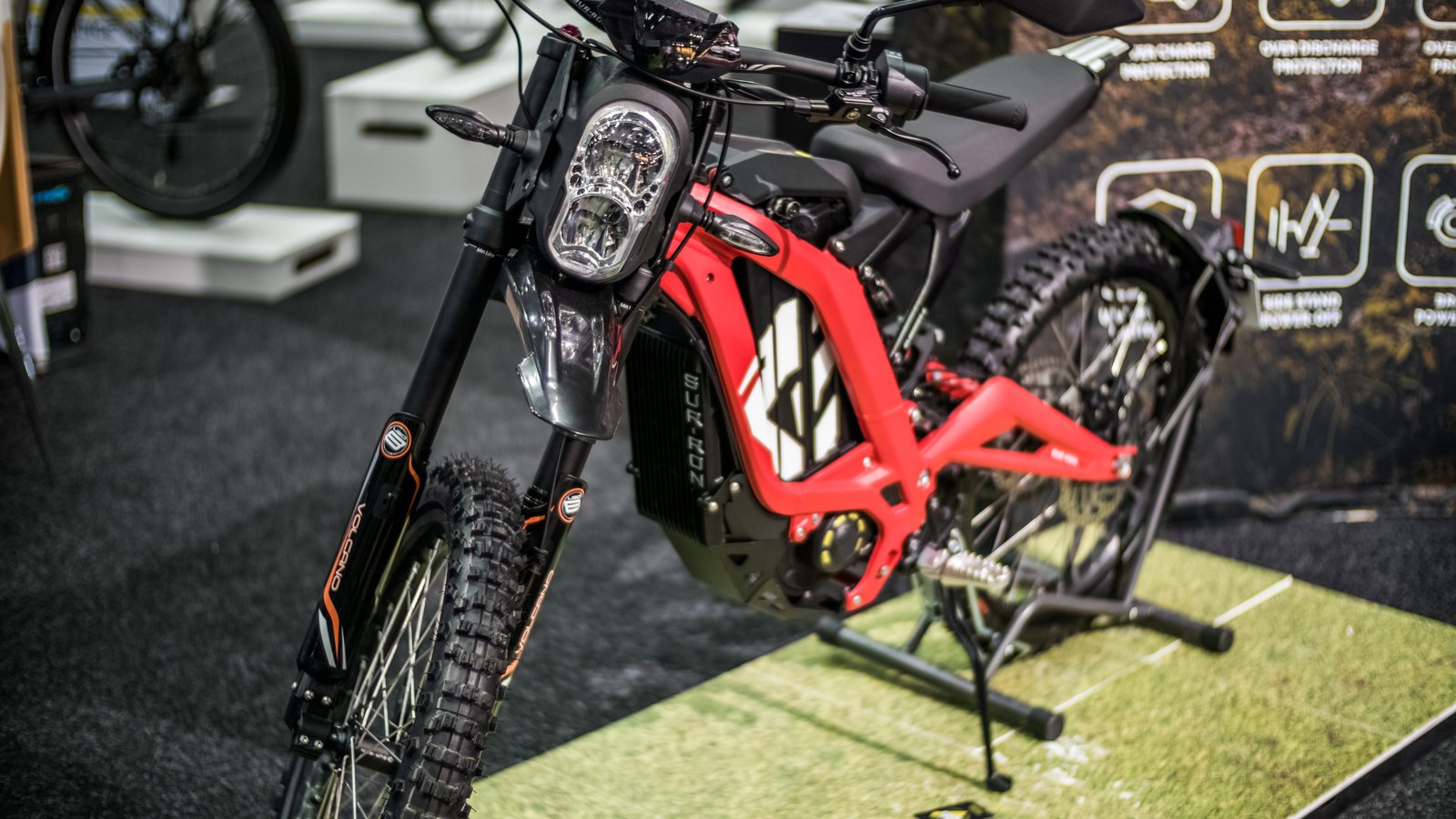 A red Sur-Ron electric dirt bike with foot pegs and no pedals on display at a trade show