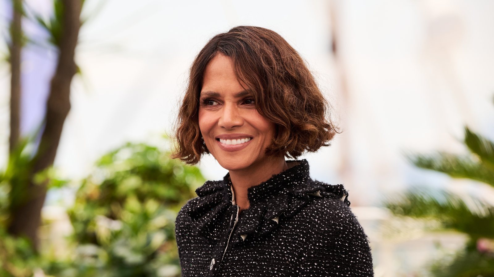 Halle Berry, with short wavy hair and a black tweed jacket, at a daytime photocall in Cannes