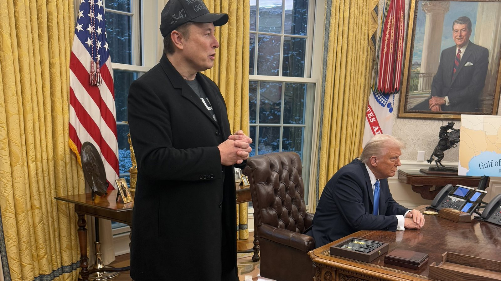 Elon Musk stands in the Oval Office while President Donald Trump sits at the Resolute Desk