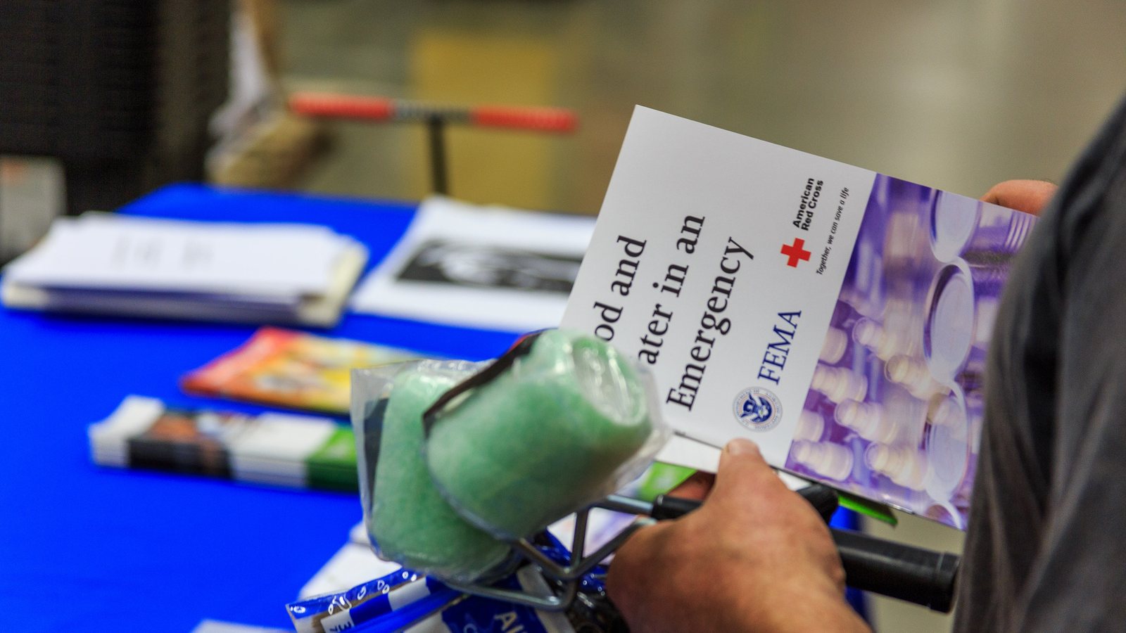 A shopper holds a FEMA and American Red Cross brochure titled Food and Water in an Emergency at a preparedness display in a hardware store