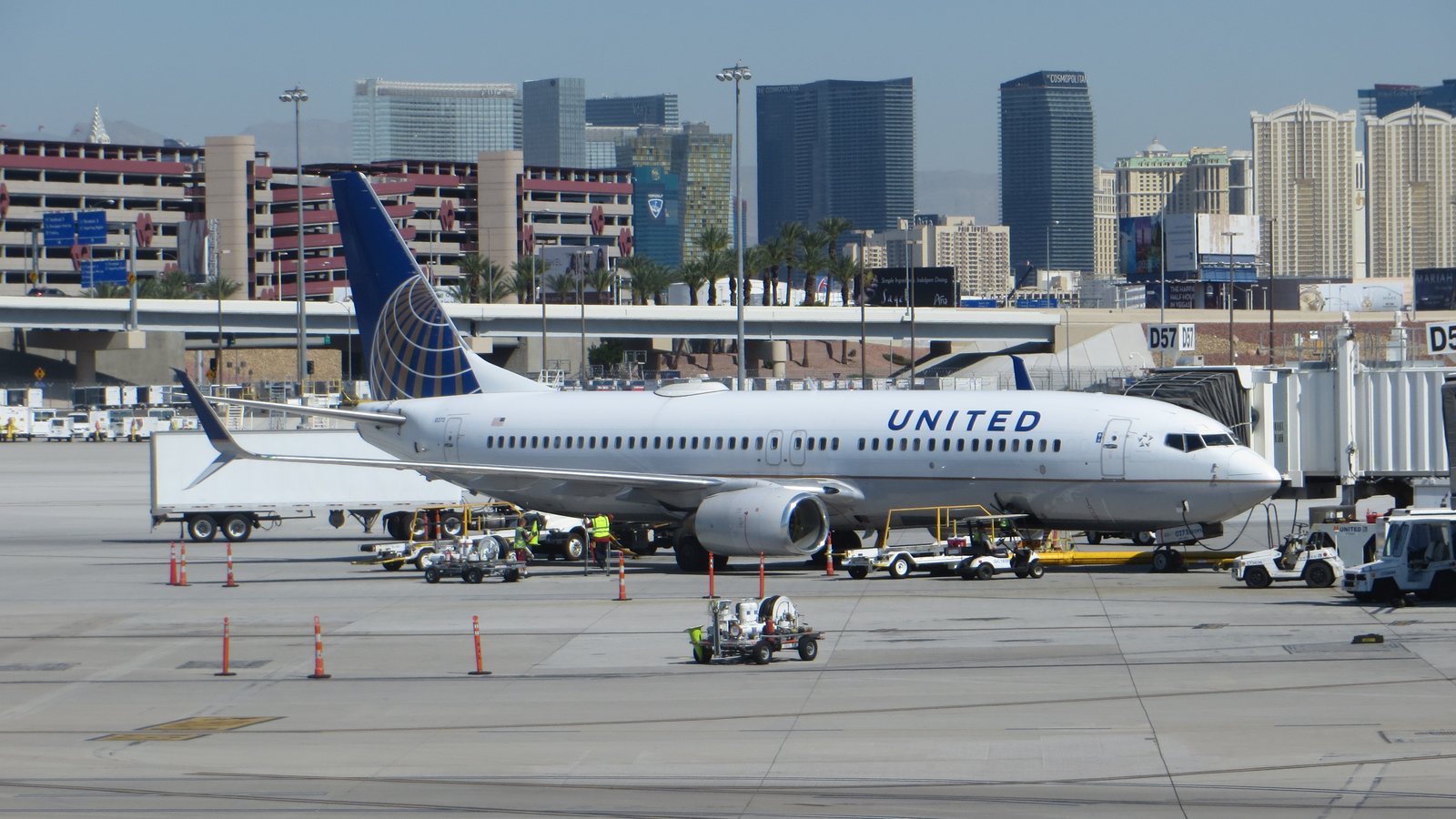 A white United Airlines Boeing 737 with a blue globe tail parked at a gate at the Las Vegas airport, with Strip hotel towers behind it